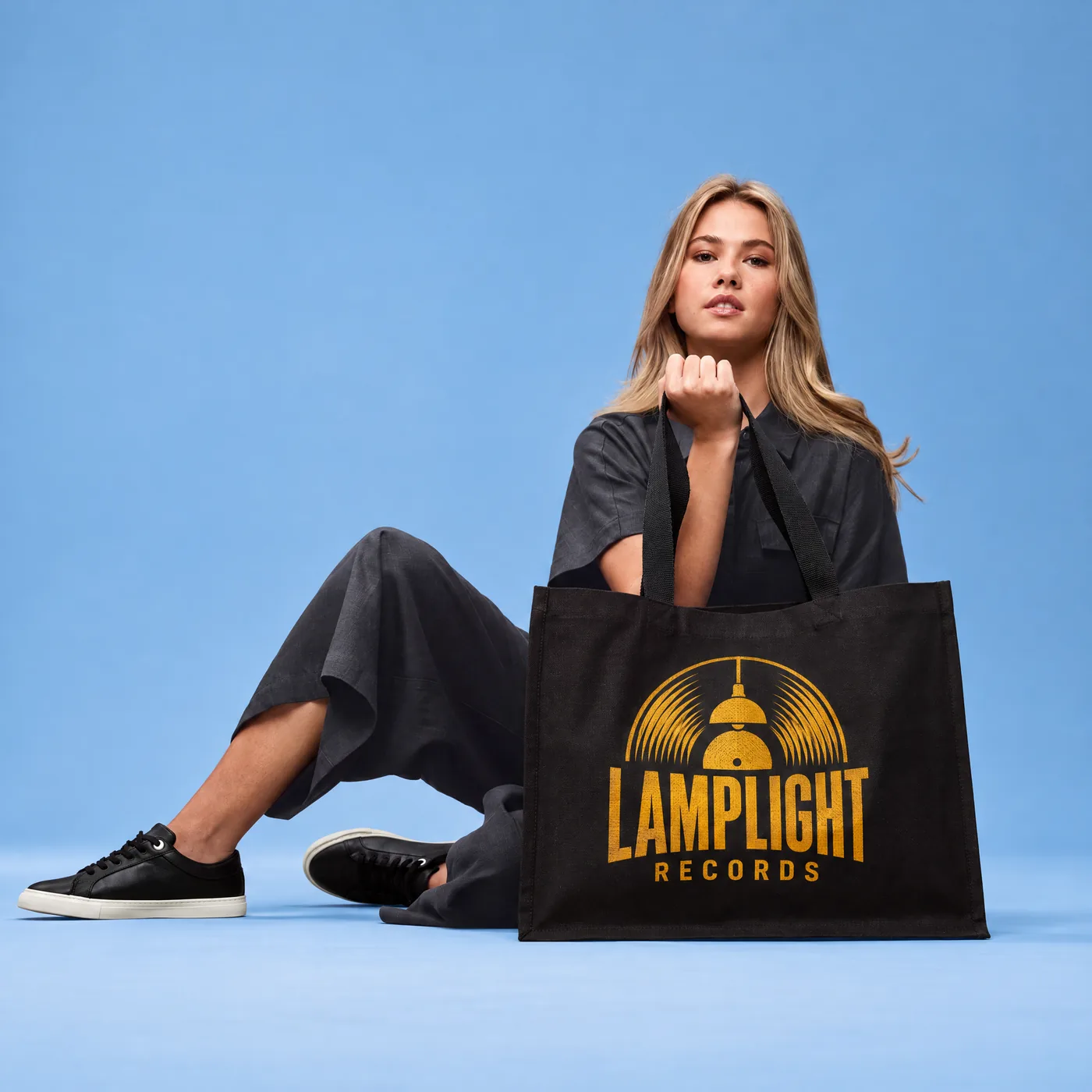 Woman sitting beside a black canvas tote printed with a record shop logo in gold