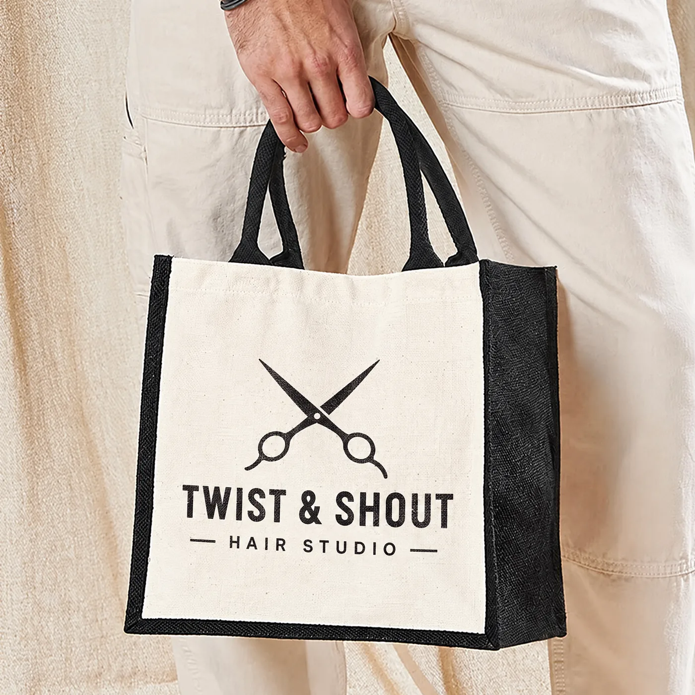 Jute bag with black sides and handles printed with a pair of scissors and a hair studio name in black