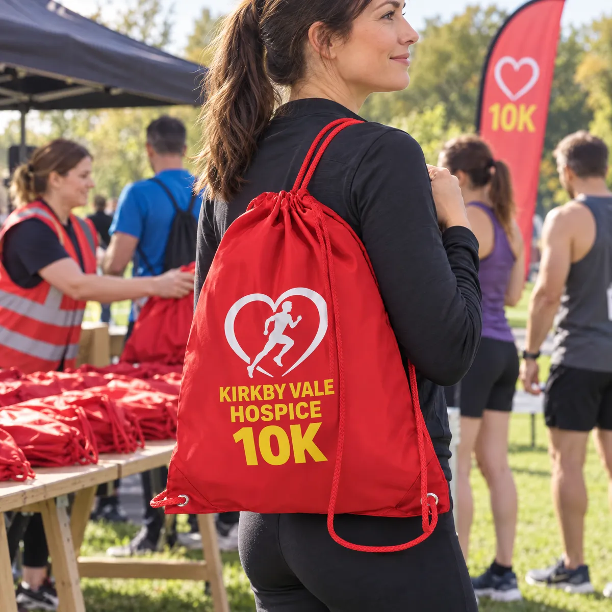 Red polyester drawstring bags printed with a charity 10K logo, laid out on tables for runners to collect