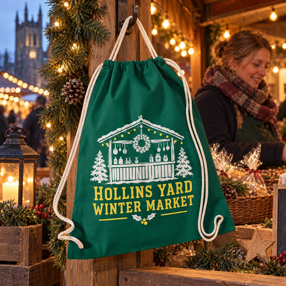 Bottle green cotton drawstring bag printed with a Christmas market logo, hanging on a lit market stall