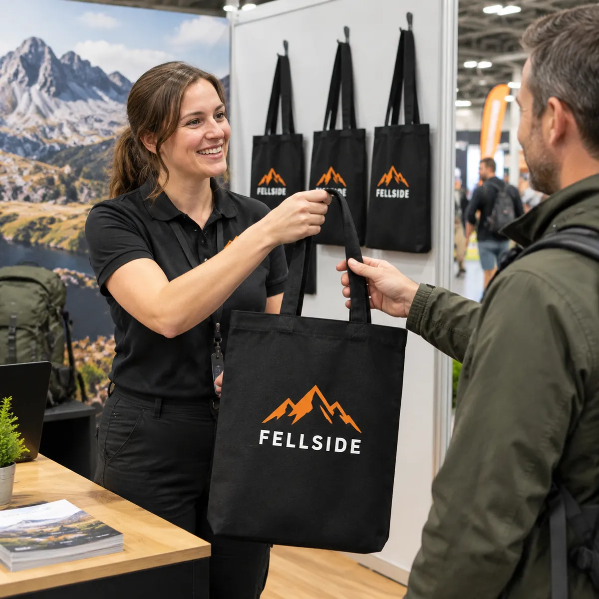 Black recycled canvas tote bags printed with an outdoor brand logo, hanging on an exhibition stand