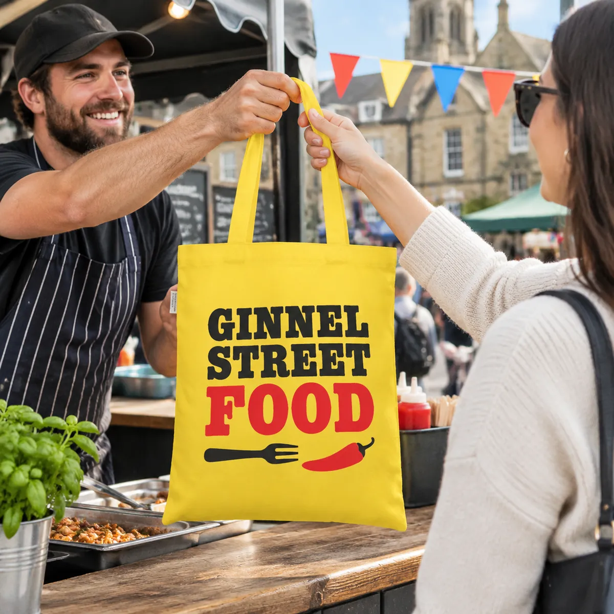 Yellow tote printed with a Ginnel Street Food Festival logo in black and red, handed over at a food stall