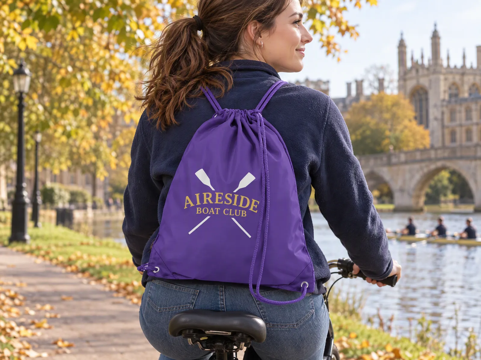 Student cycling across campus with a purple drawstring bag printed with a rowing club crest