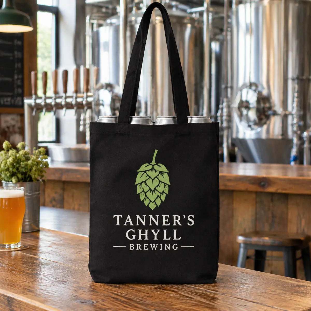 Black canvas tote printed with a green hop and white brewery name on a taproom bar
