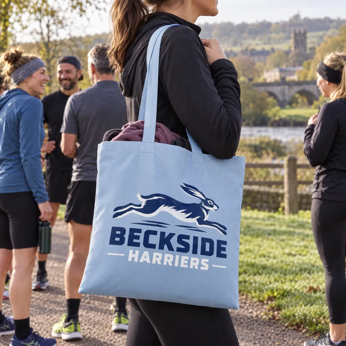 Sky blue cotton shopper printed with a Beckside Harriers logo, carried by a club runner in a park